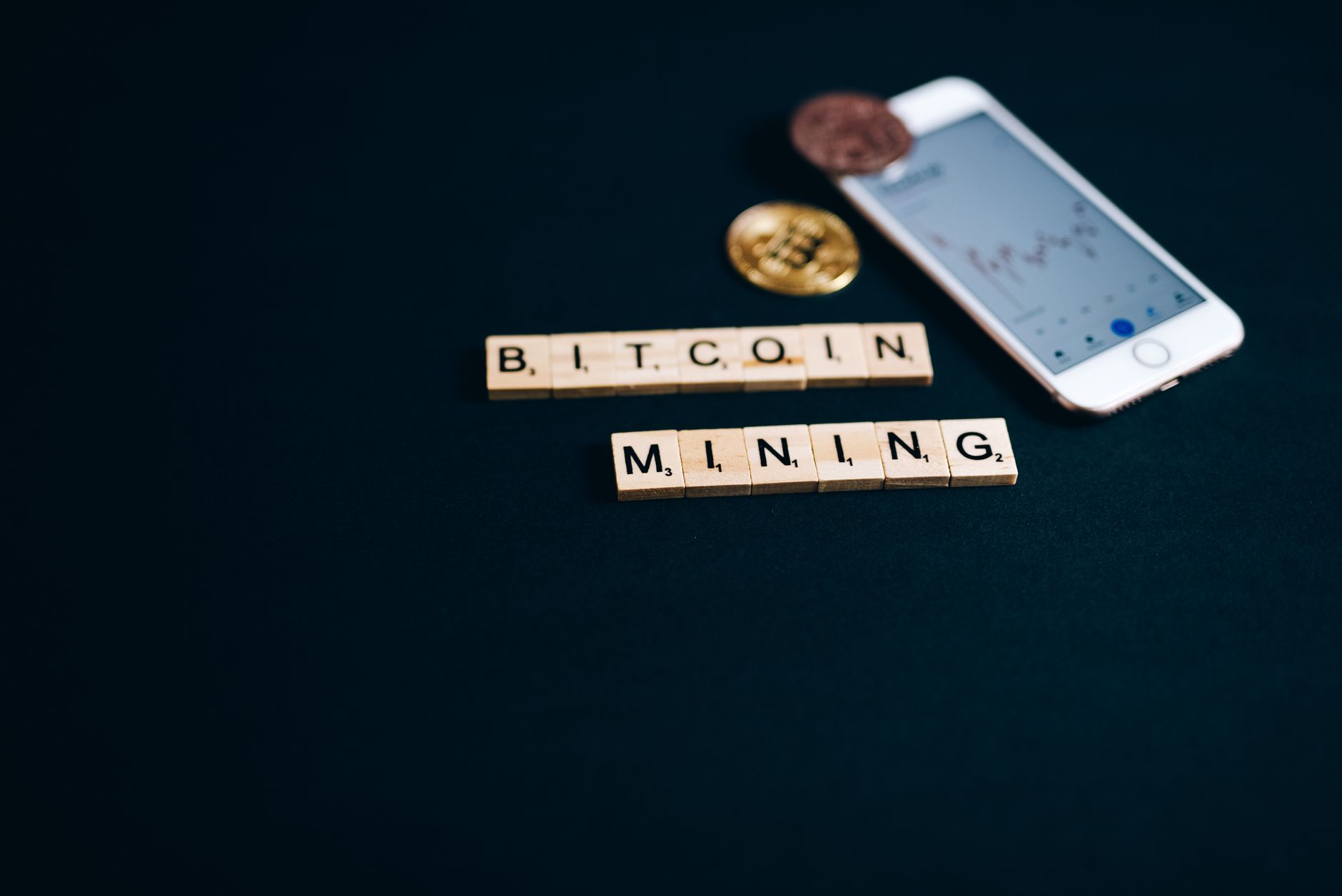 Tuiles Scrabble épelant Bitcoin Mining avec un smartphone et des pièces sur fond sombre.