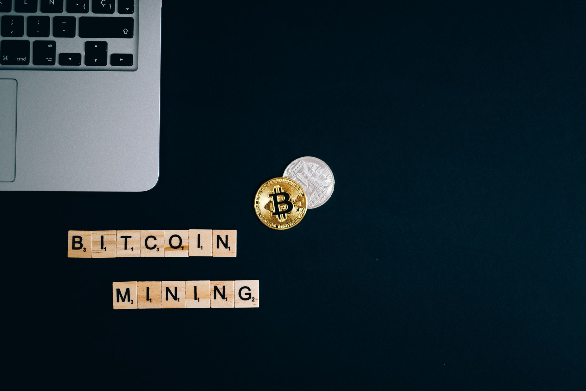 Vue de dessus d'un ordinateur portable avec des pièces de Bitcoin et des blocs formant l'inscription « Bitcoin Mining » sur une surface sombre.