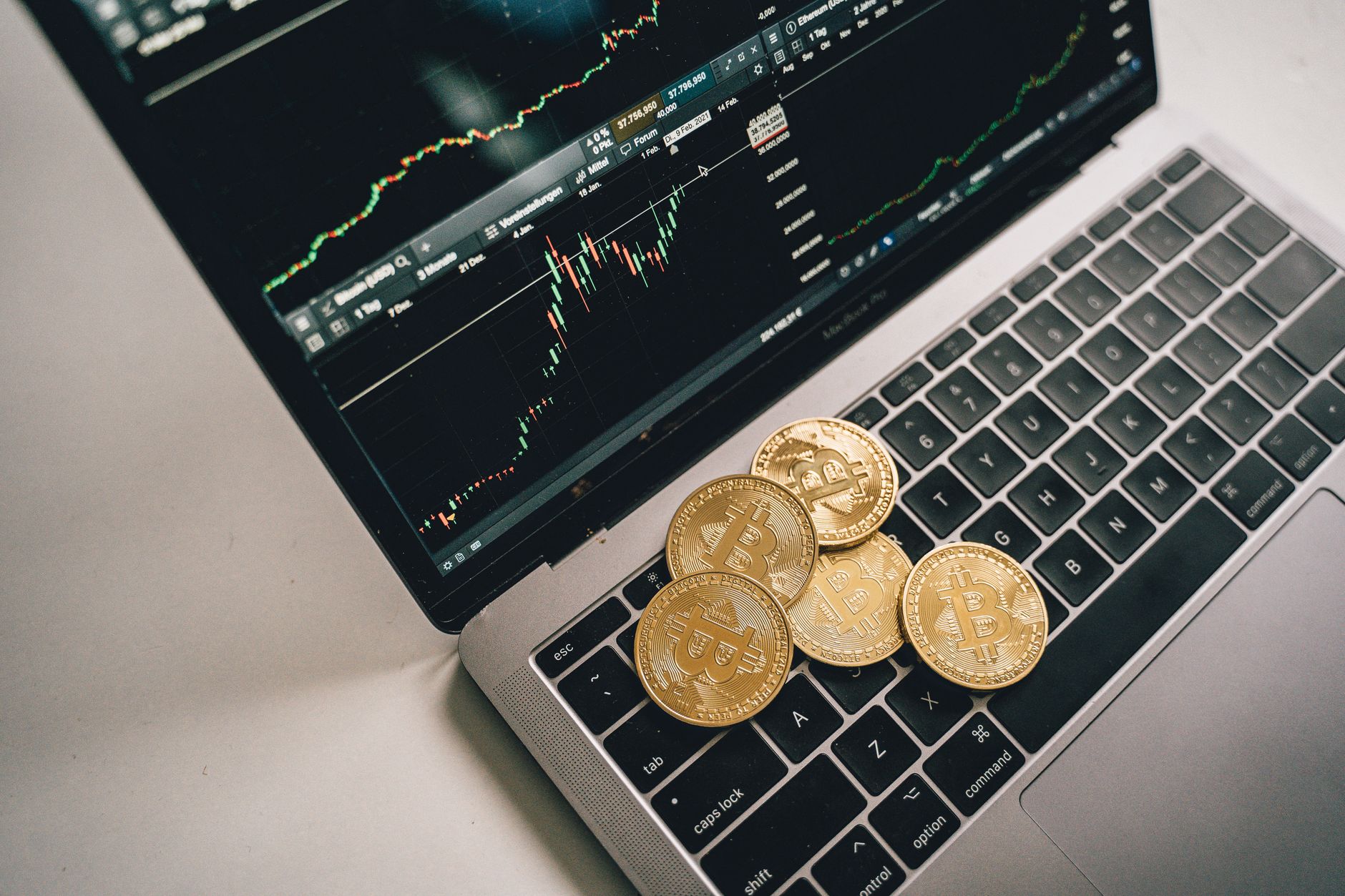 Pièces de bitcoin en or placées sur un clavier d'ordinateur portable avec un graphique de trading affiché à l'écran.