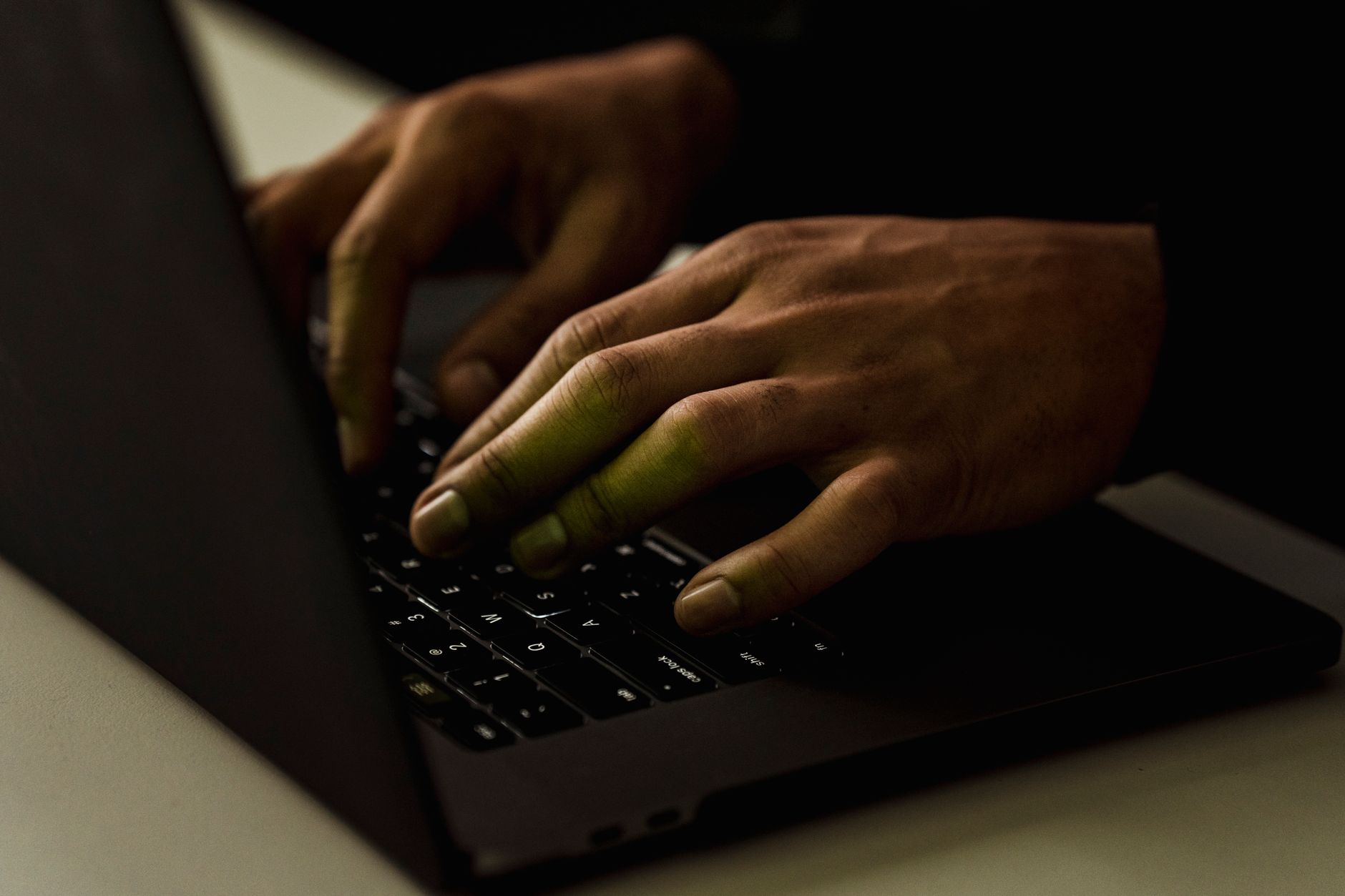 Deux mains tapent sur le clavier rétroéclairé d’un ordinateur portable dans une pièce sombre.