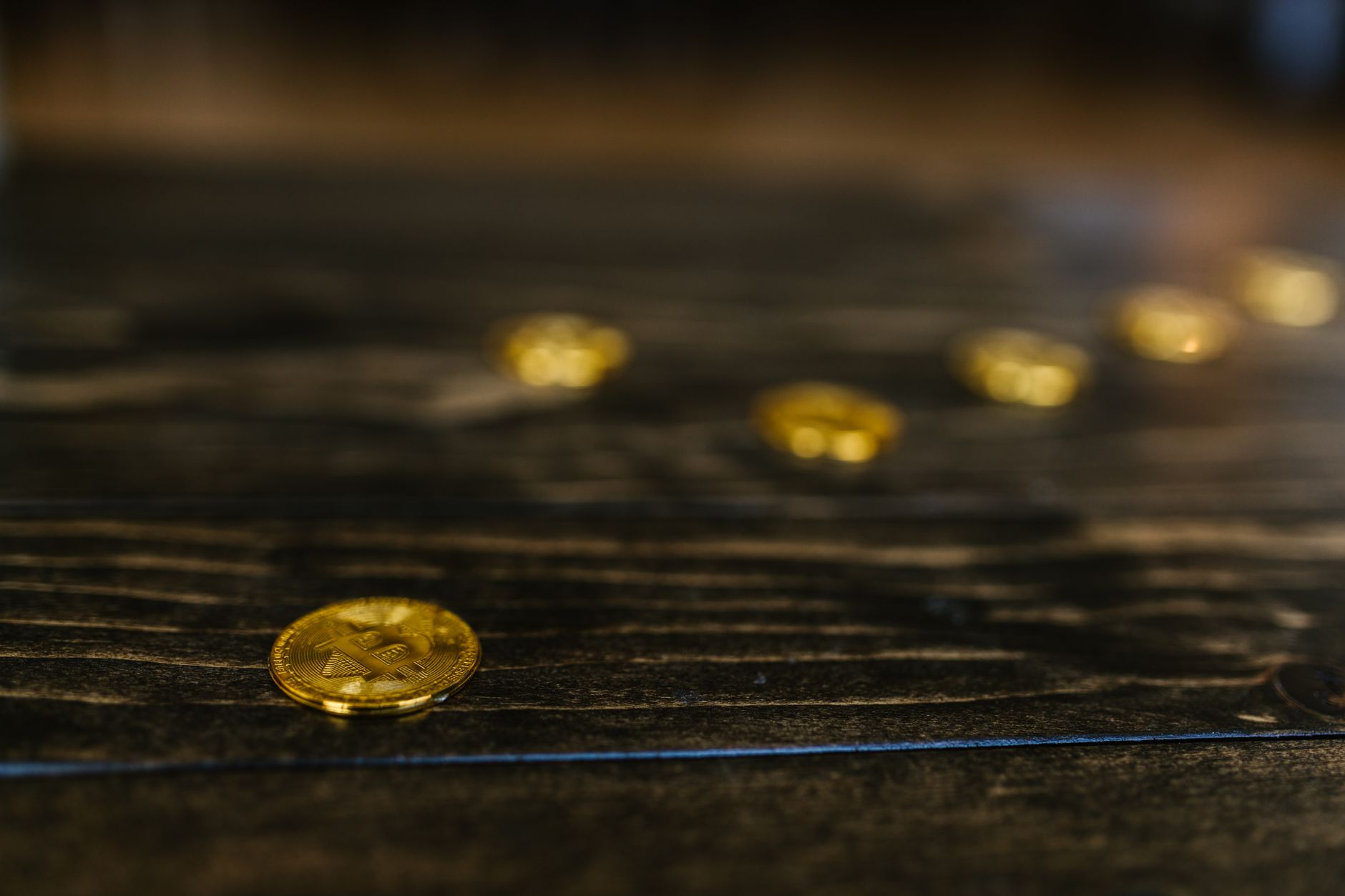 Pièce dorée à symbole Bitcoin sur une table en bois sombre, avec d’autres pièces floues en arrière-plan.